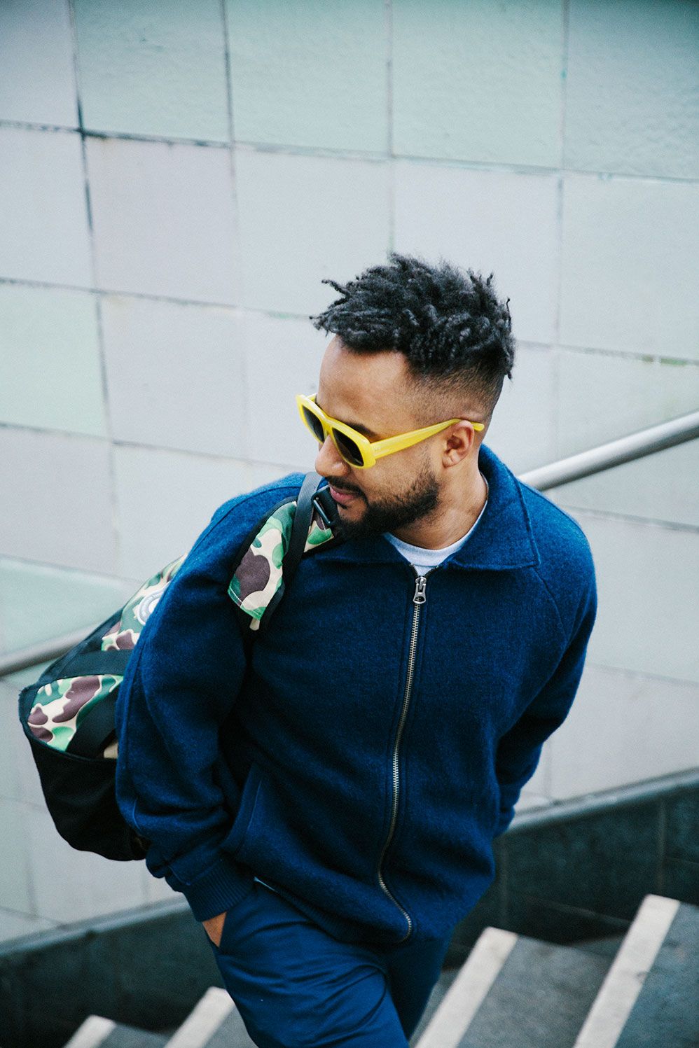 Nico Adomako in yellow Ace & Tate sunglasses on a stairway