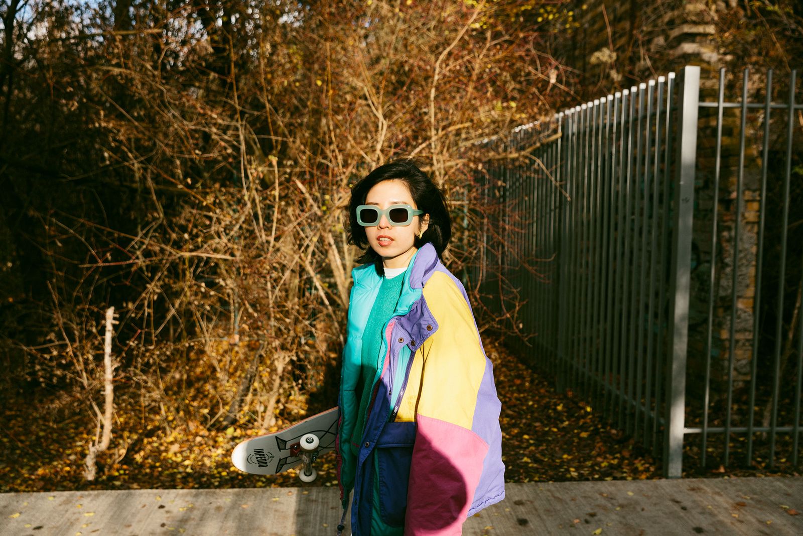 Illustrator Ruohan Wang in white Ace & Tate sunglasses and a colourful jacket outdoors in Berlin