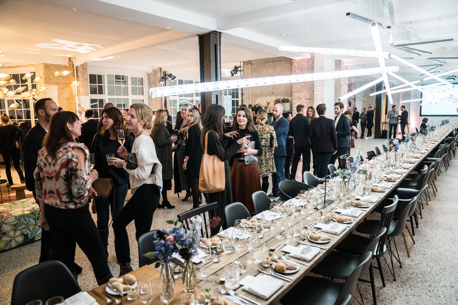 Guests gathering along a long dinner table under light sculptures at the AD Design Award in the Friends Space