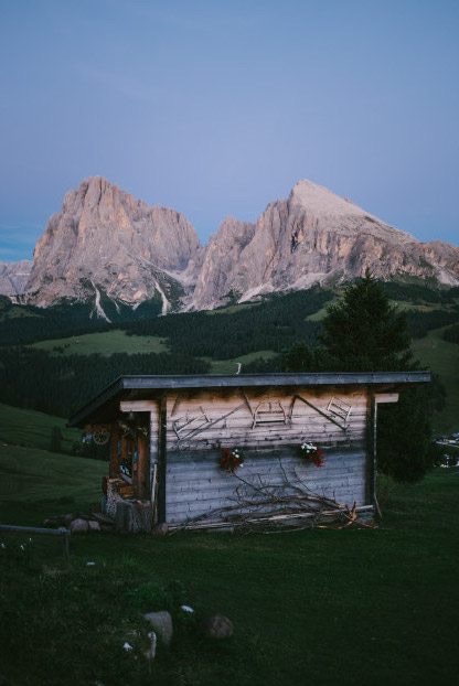 Wooden alpine hut below Dolomites peaks at dusk, adidas Journeys