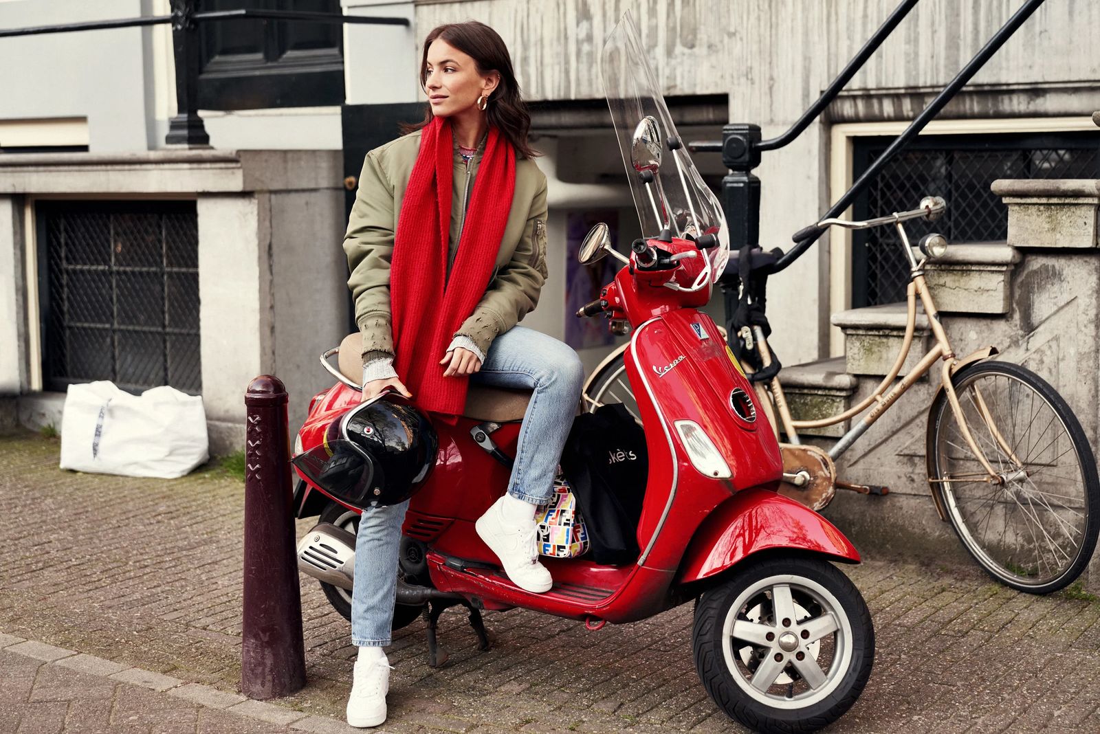 Stylist sitting on a red scooter outside an Amsterdam house, ClassPass #bethebalance editorial in Amsterdam