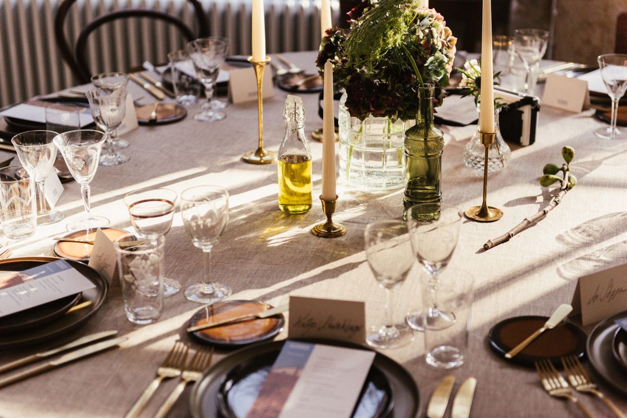 Long dinner table set with candles, olive branches and dark plates