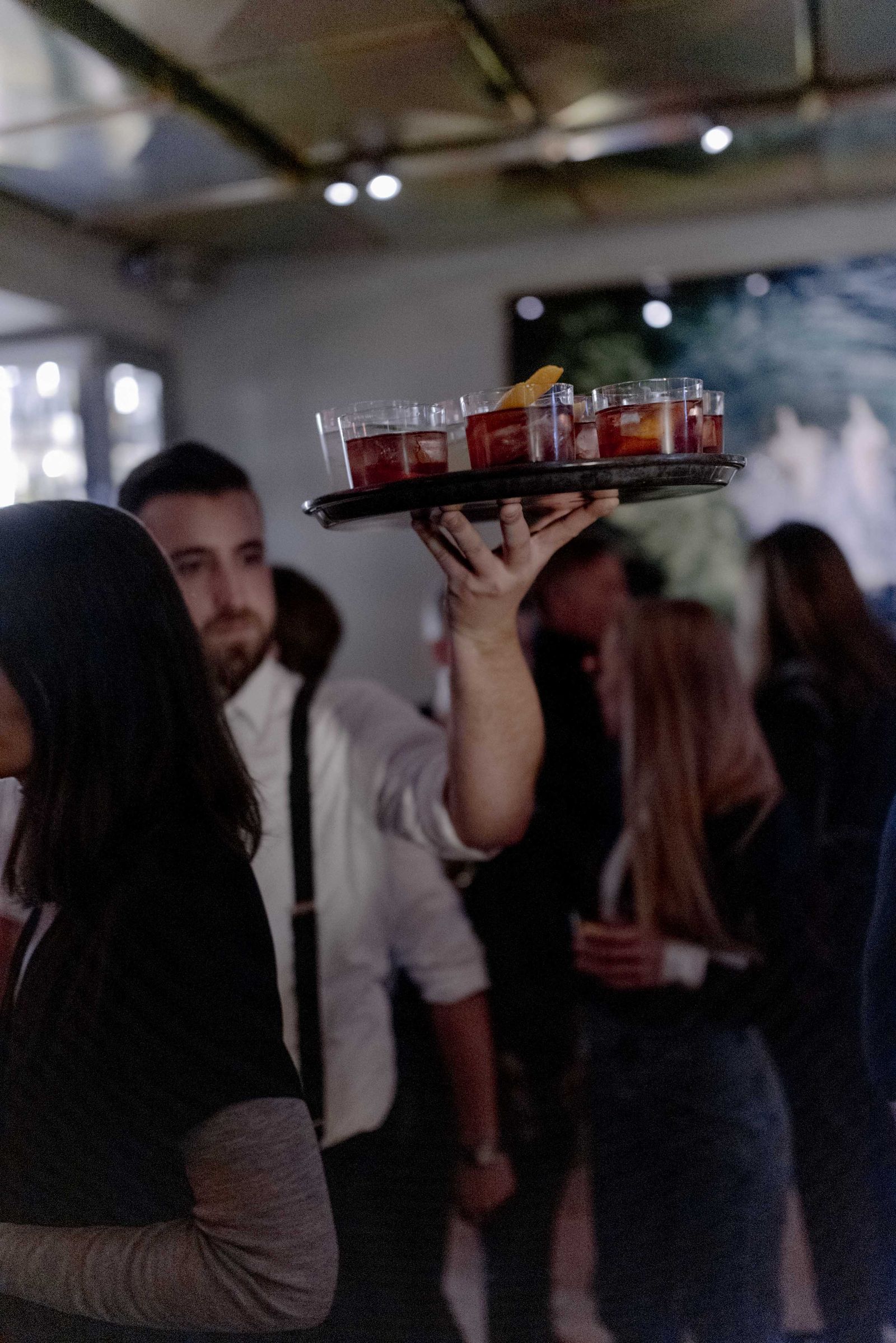 A waiter carrying a tray of drinks through the crowd at the CLOSED evening