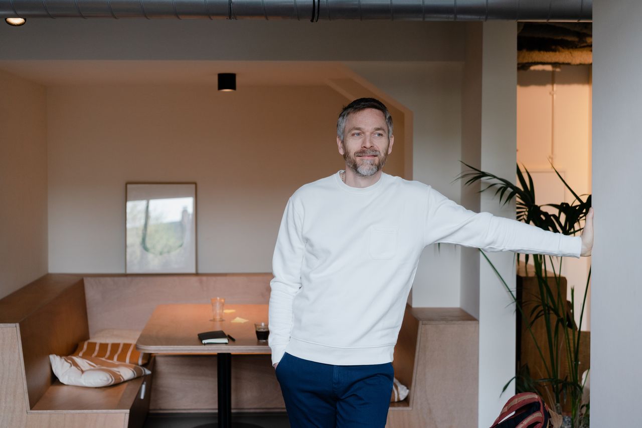 Designer in a white jumper leaning on a doorframe in his Amsterdam office