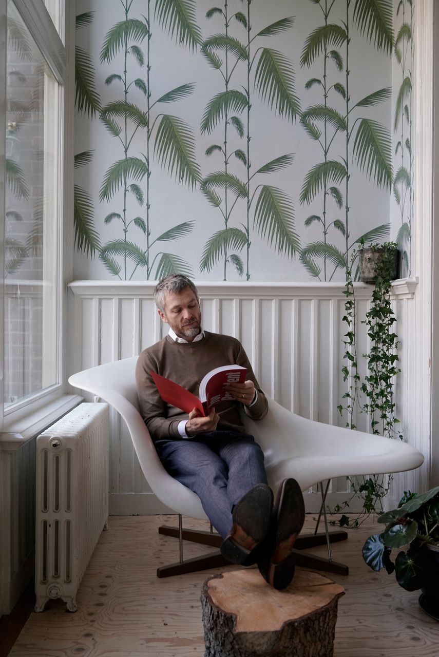Designer reading in a white lounge chair against palm-leaf wallpaper, Amsterdam