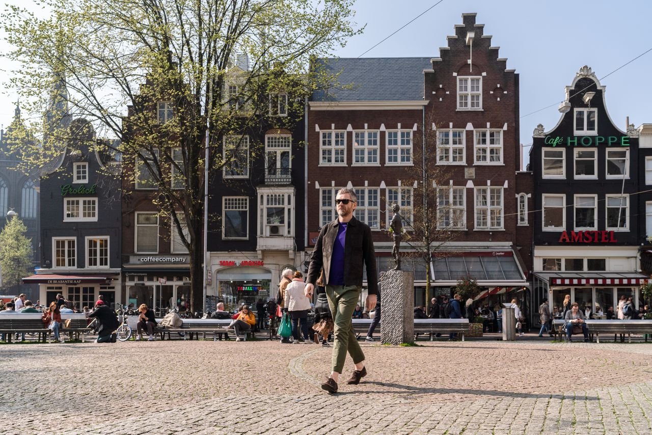 Designer crossing a square lined with gabled houses in Amsterdam