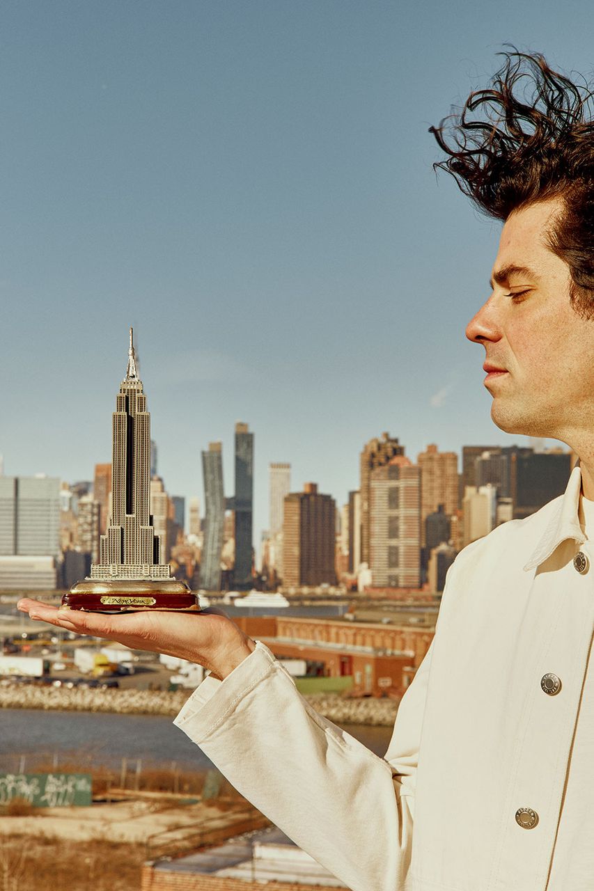 Graphic designer holding a small model of the Empire State Building against the Manhattan skyline