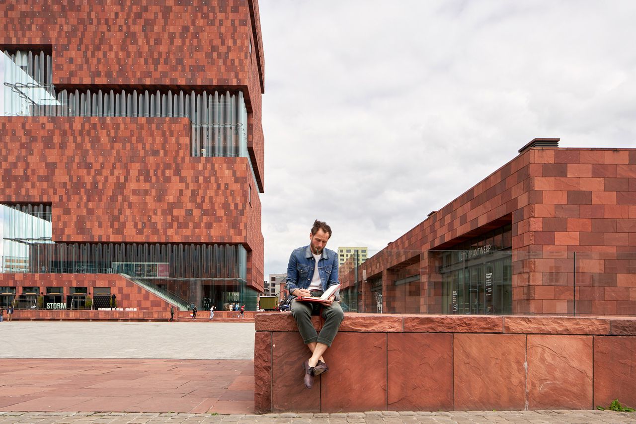 Painter sitting on a red stone wall below the MAS museum in Antwerp