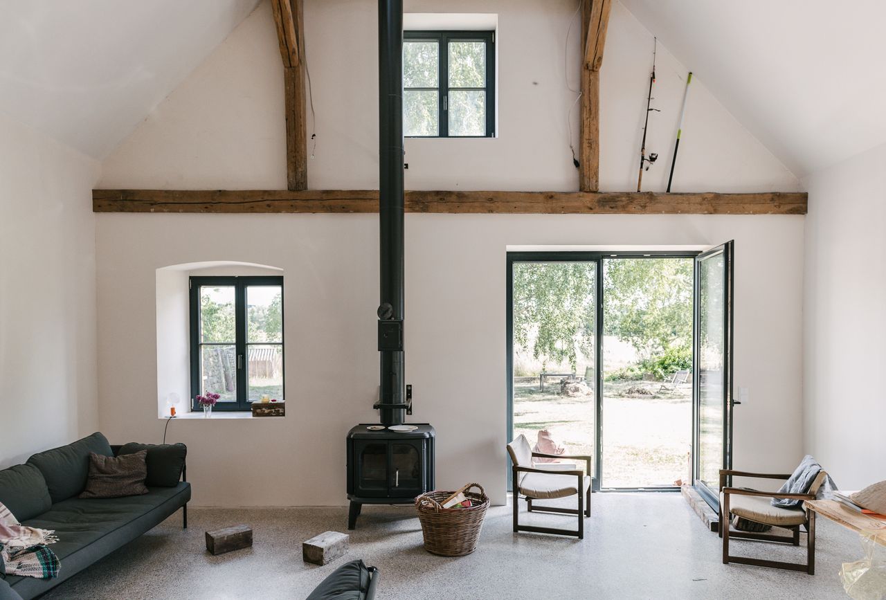 White living room with a wood stove and exposed beams in a renovated country house, Uckermark