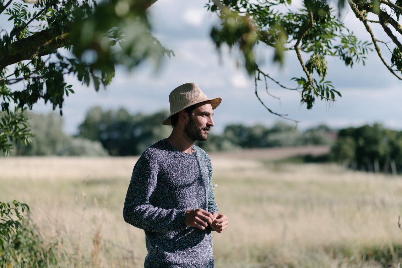Photographer in a straw hat and knitted jumper standing in a meadow under a tree, Uckermark