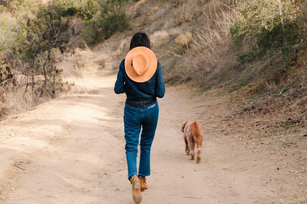 Stylist in a wide hat walking a dirt trail in Laurel Canyon with her dog