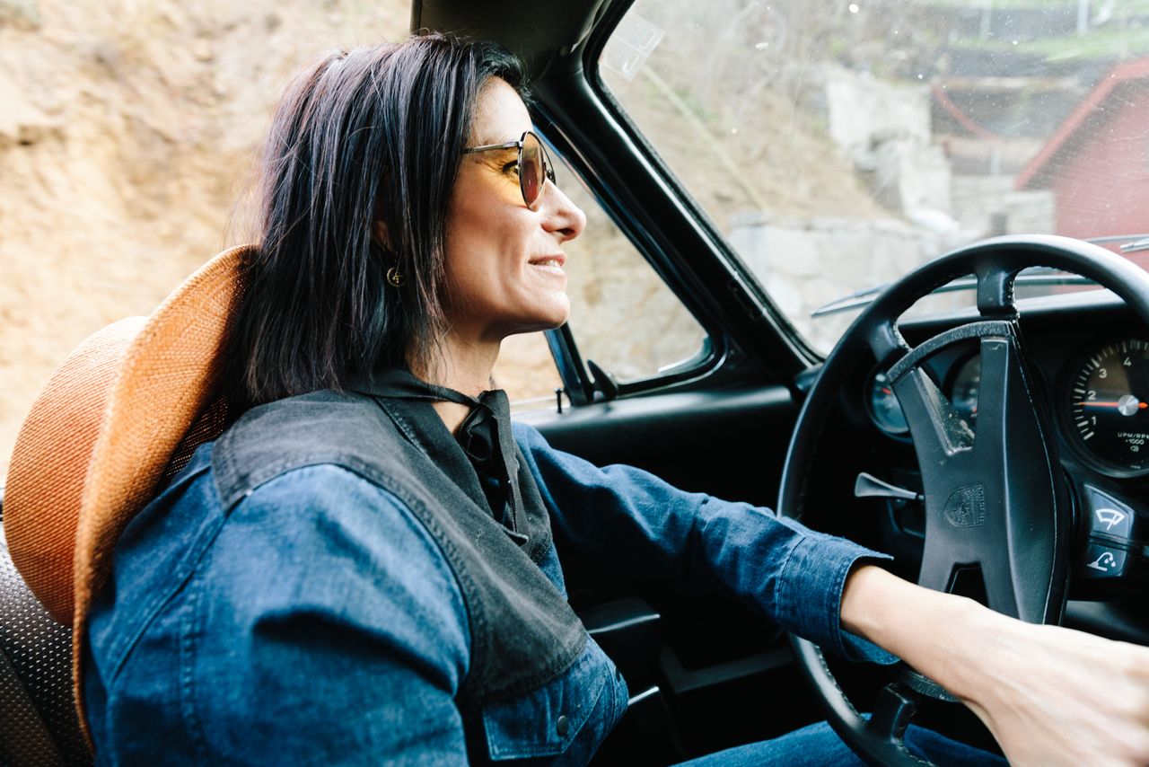Stylist in a denim jacket and sunglasses driving a vintage convertible, Los Angeles