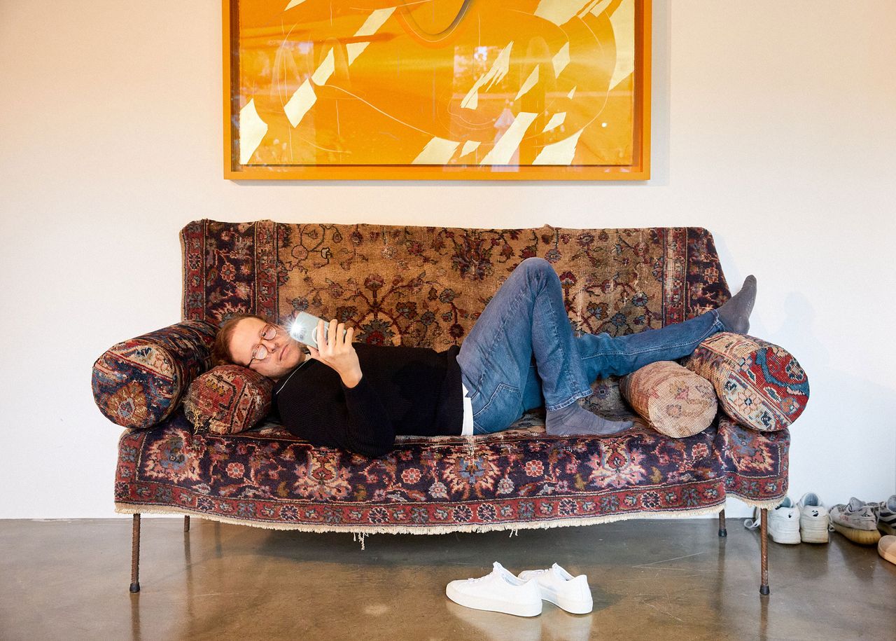 Gallerist resting on a patterned sofa below an orange painting in his Berlin apartment