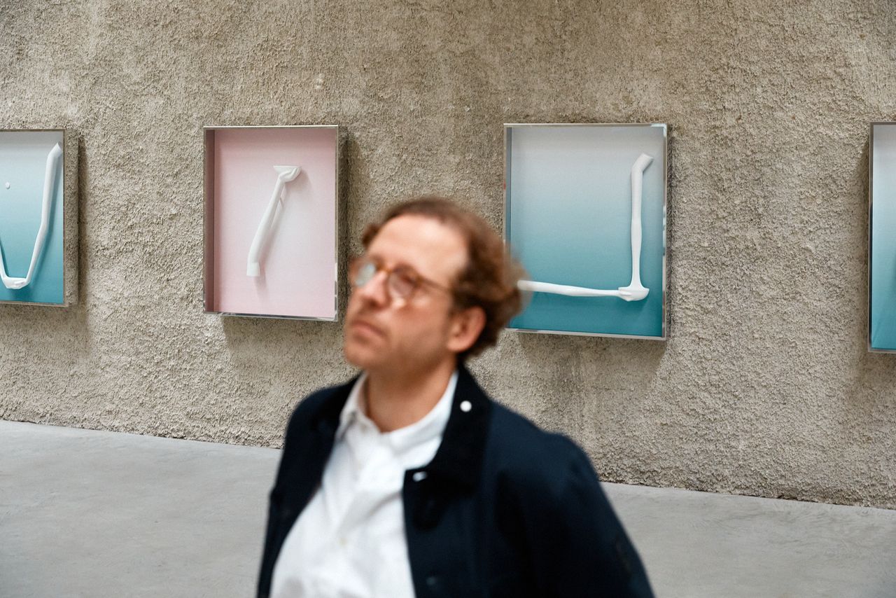 Gallerist in a dark jacket in front of wall-mounted artworks in the gallery, Berlin
