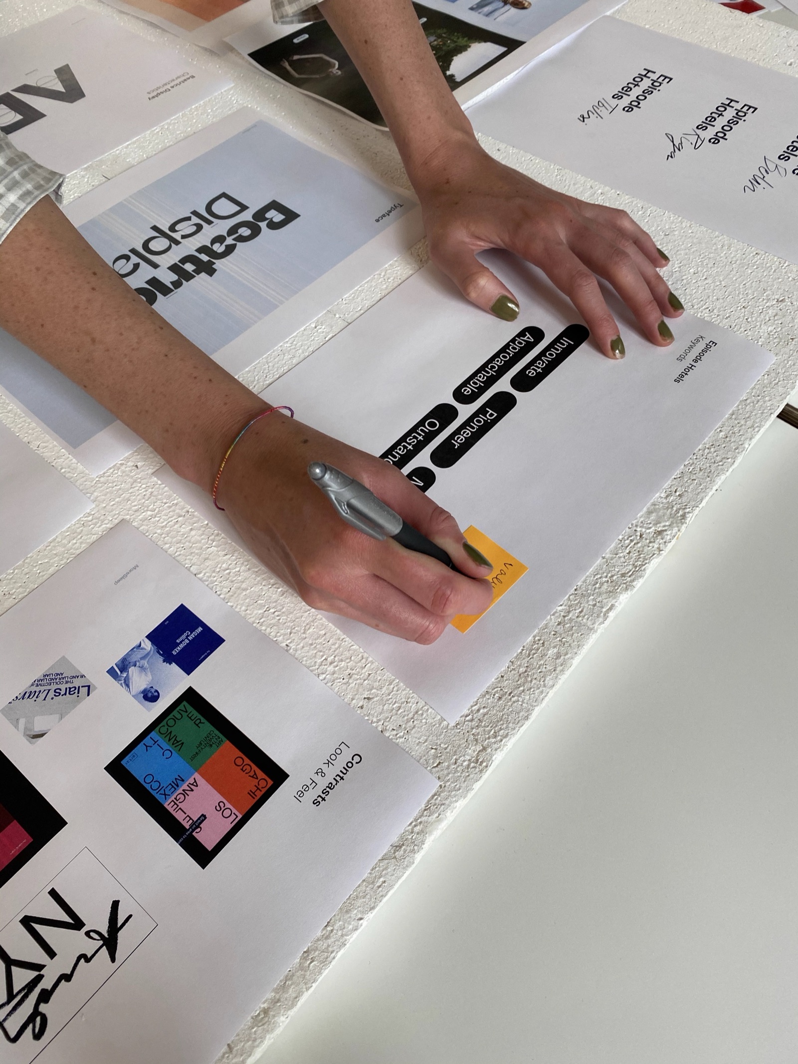 Hands marking up printed Episode Hotels identity sheets on a table