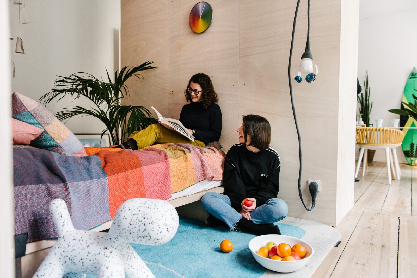 Two women reading on a bed with a colourful blanket in the Friends Apartment