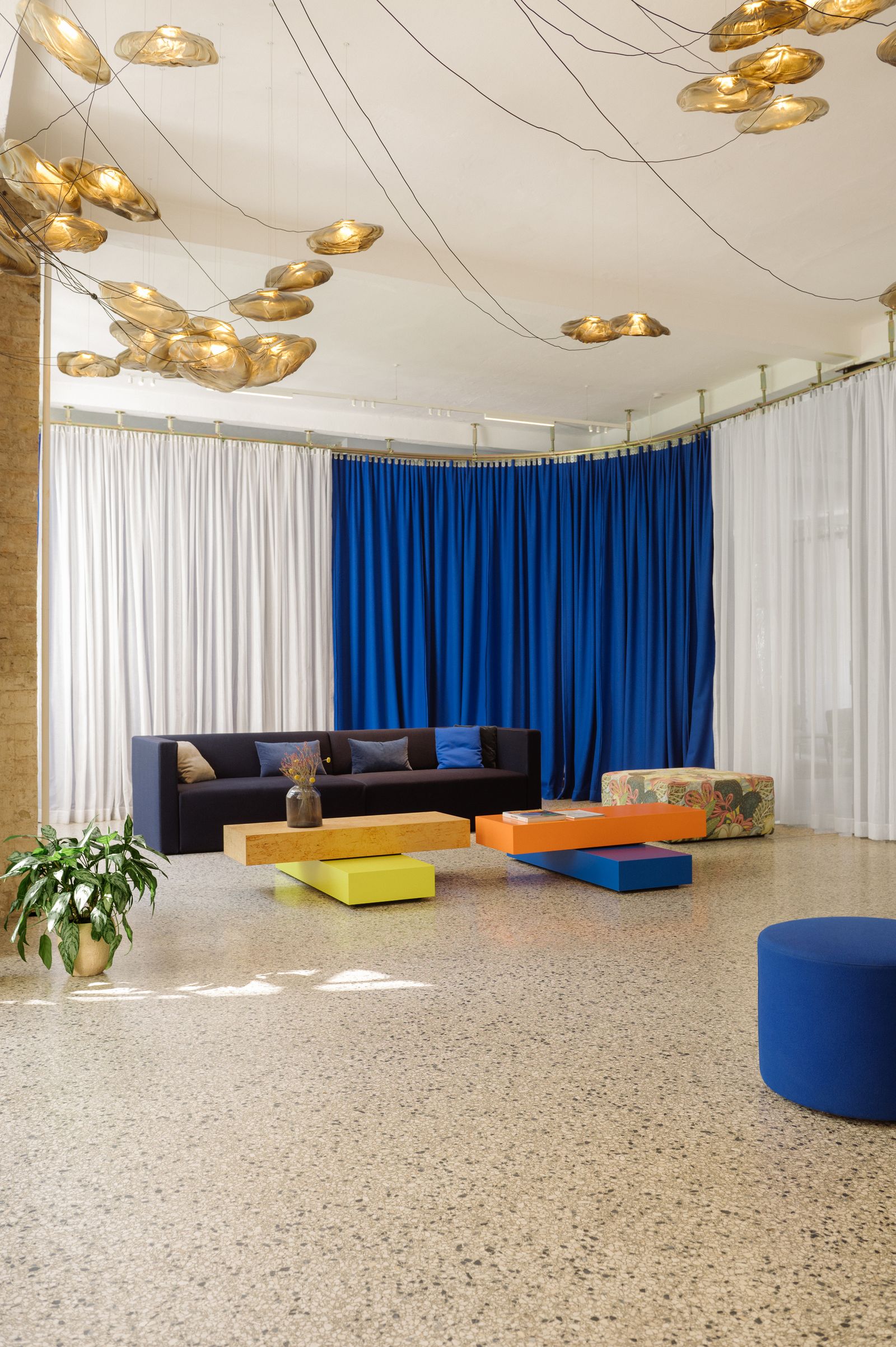 Lounge with blue and white curtains, dark sofas and colourful block tables in the Friends Space, 2024