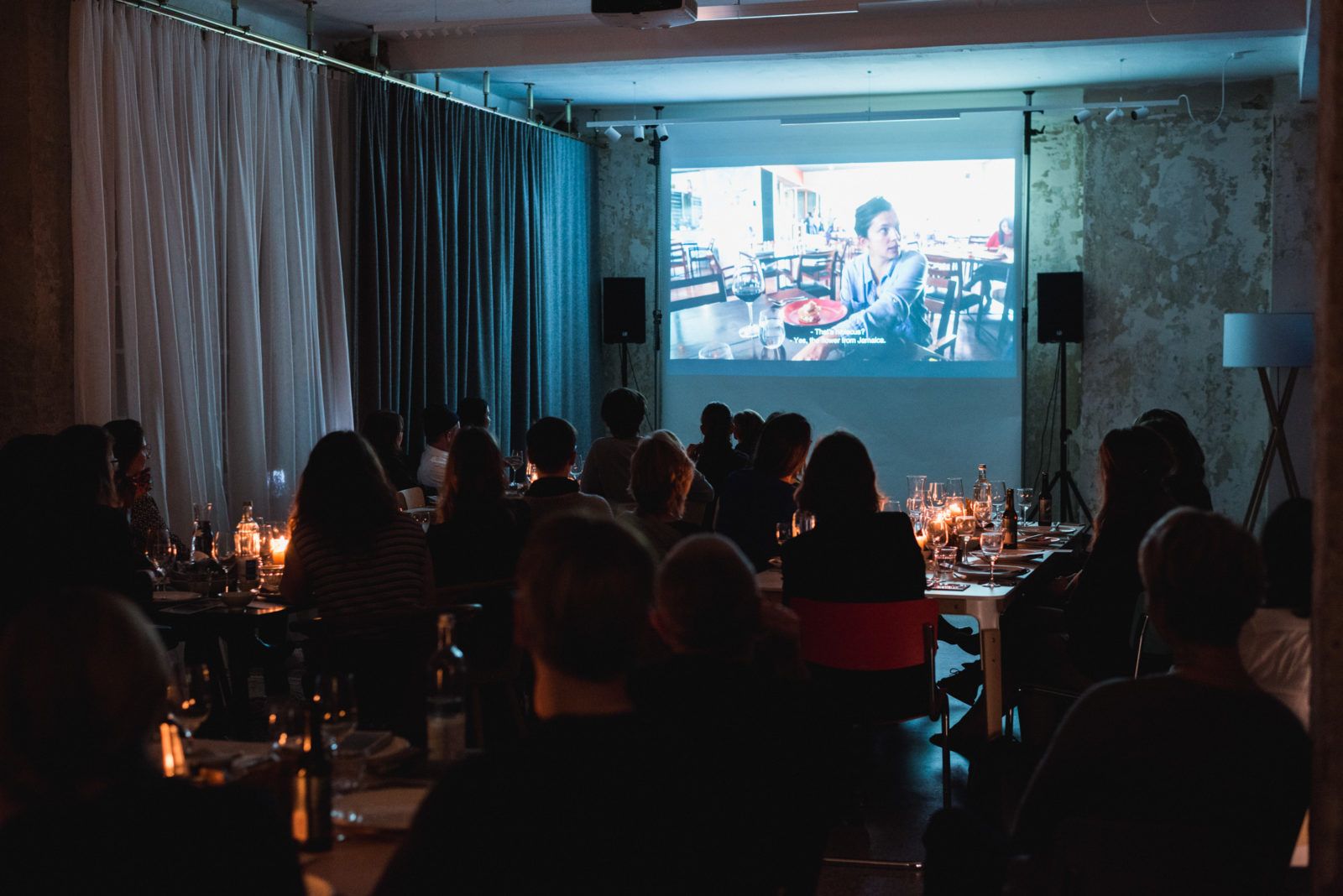 Guests at candlelit tables watching a film at the Clam Club supper club, Friends Space