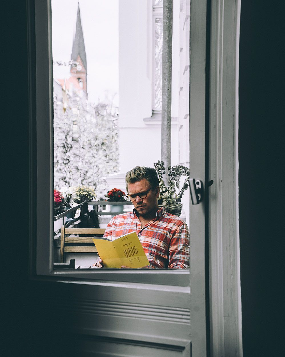 Furniture designer reading a yellow booklet at an open window in Berlin