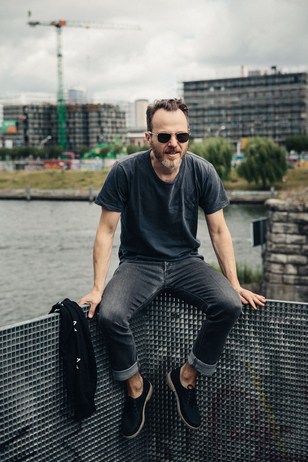 Photographer sitting on a railing by the Spree with cranes and new buildings behind