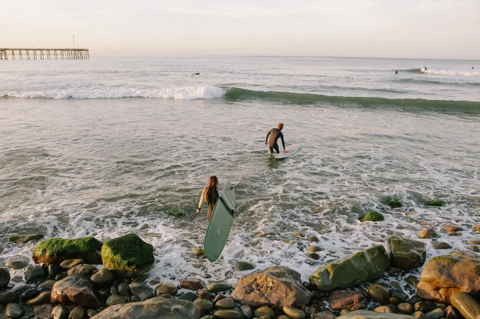 Two surfers walking into the sea over rocks, Friends of Friends brand image