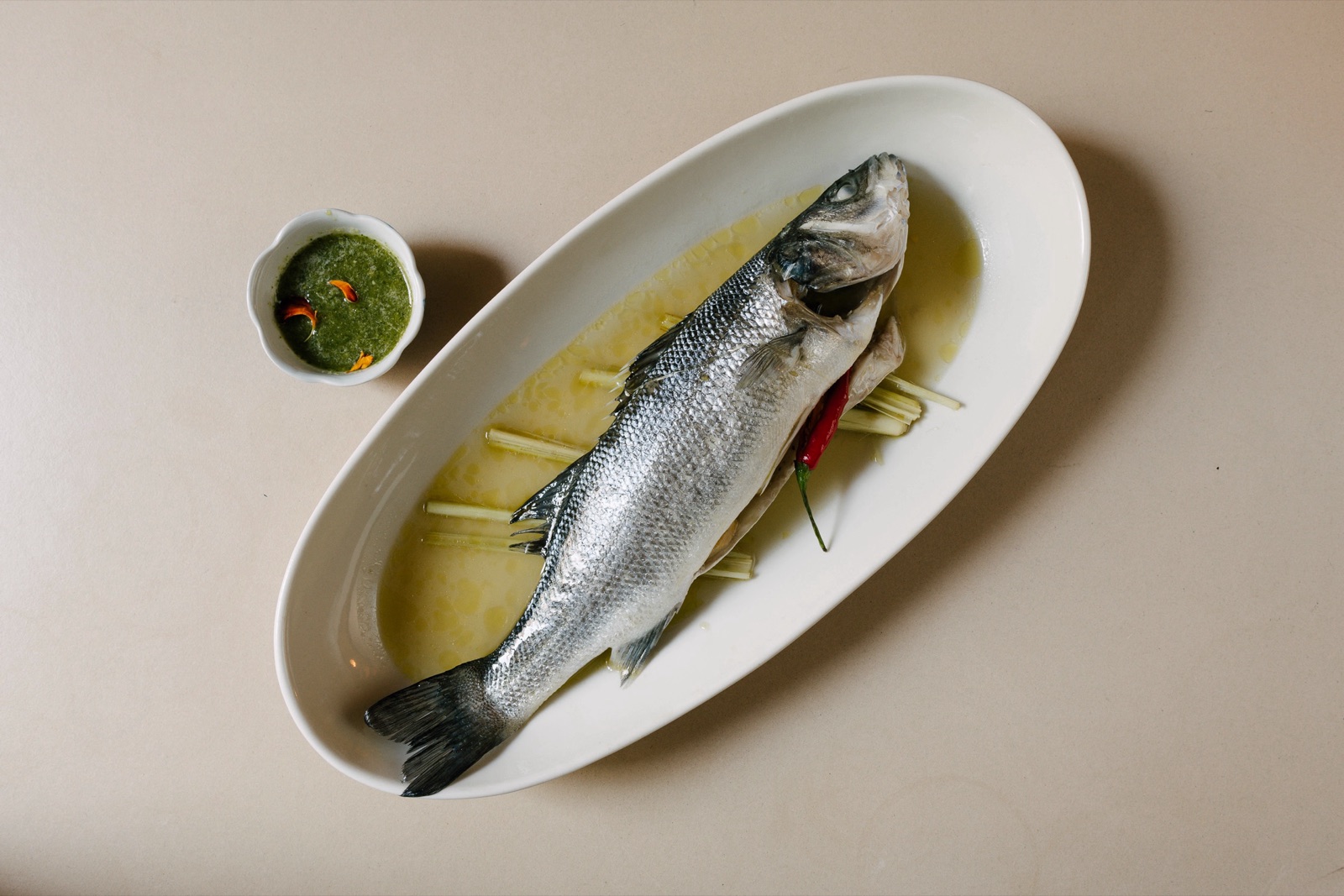 Whole steamed fish with green sauce on an oval plate at Kin Dee