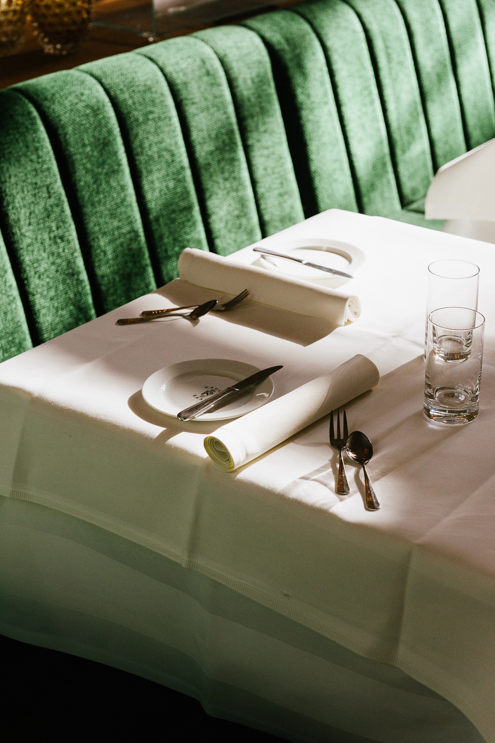 Table set with white linen beside a green velvet banquette at Pauly Saal