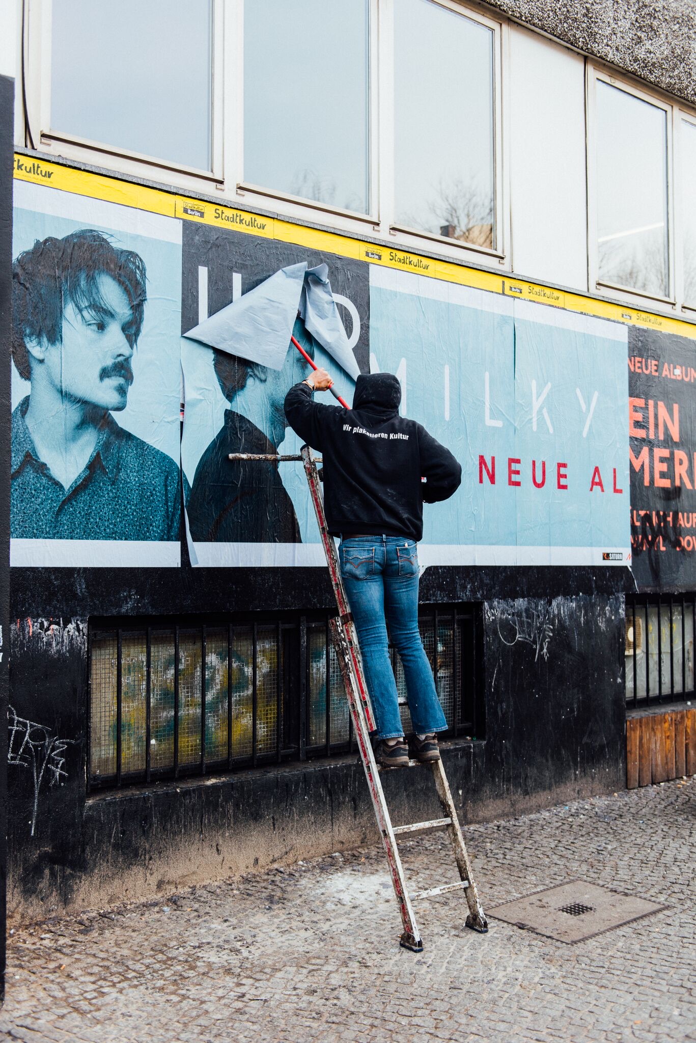 Poster paster on a ladder at a Berlin billboard, You, Me & Berlin campaign photography
