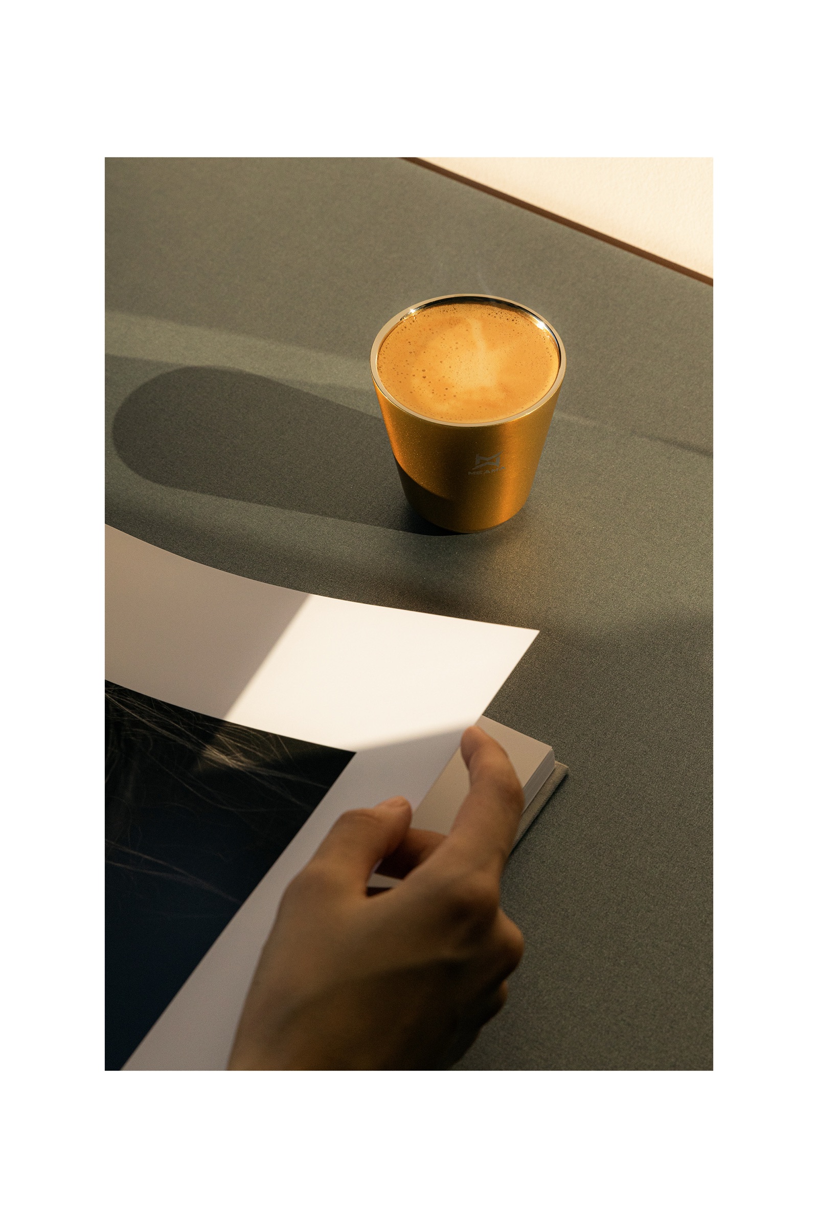 Meama poster with a gold coffee cup on a table in sunlight