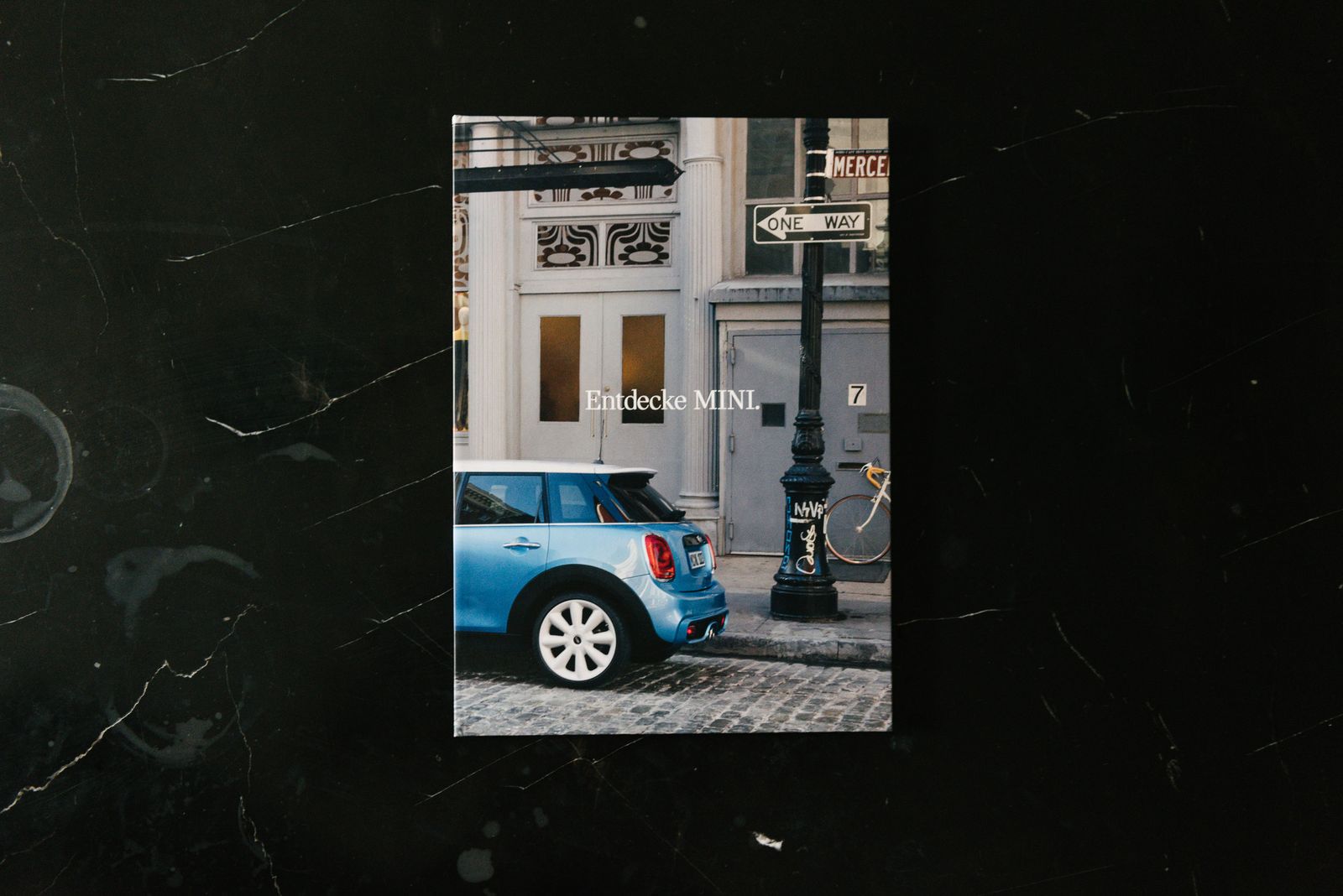 MINI Lookbook cover with a blue MINI on a city street, on black marble