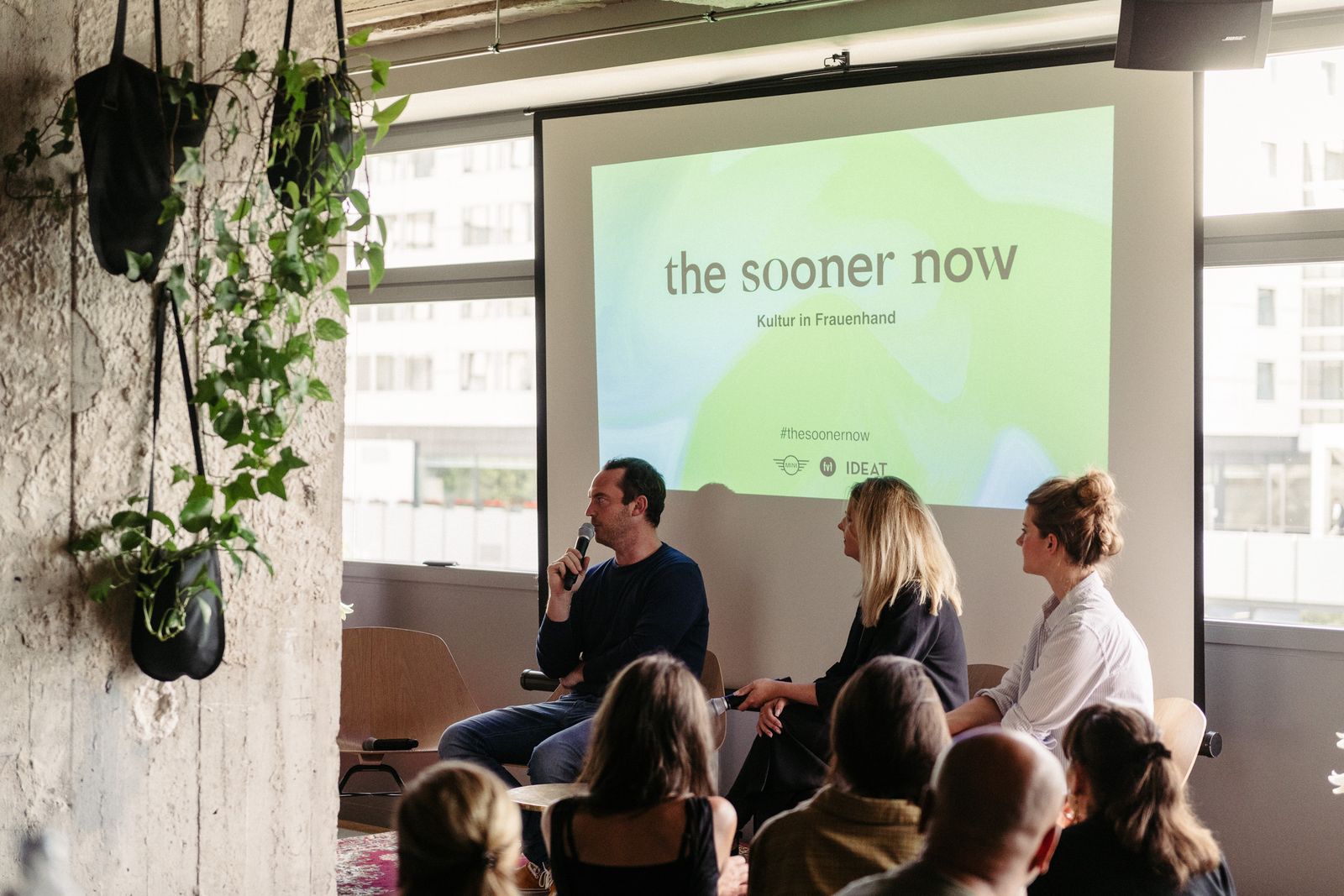 Speakers in front of a screen reading The Sooner Now, Kultur in Frauenhand, with MINI, FvF and IDEAT logos