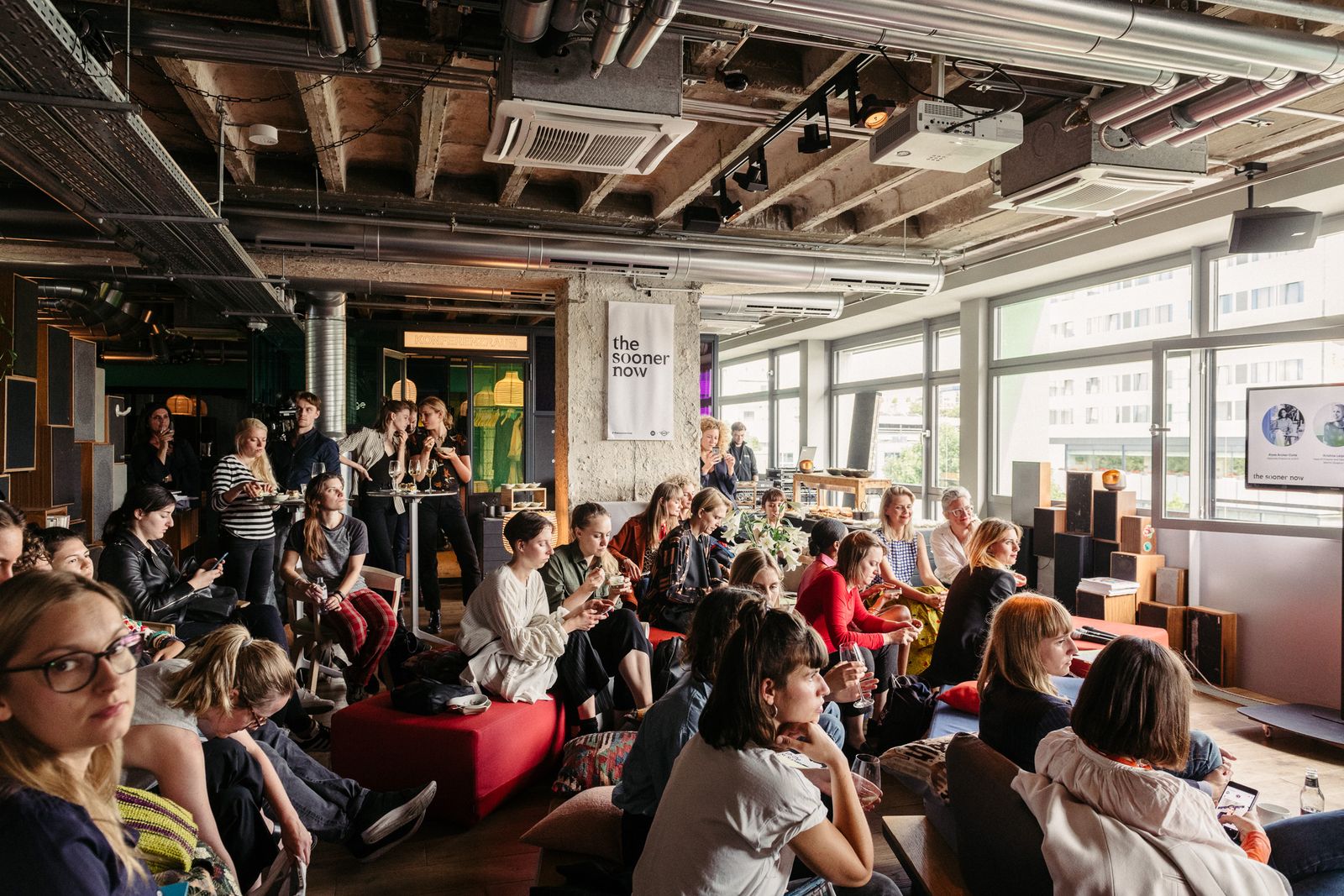 Audience on sofas and cushions in a concrete loft for The Sooner Now talk, Berlin 2018