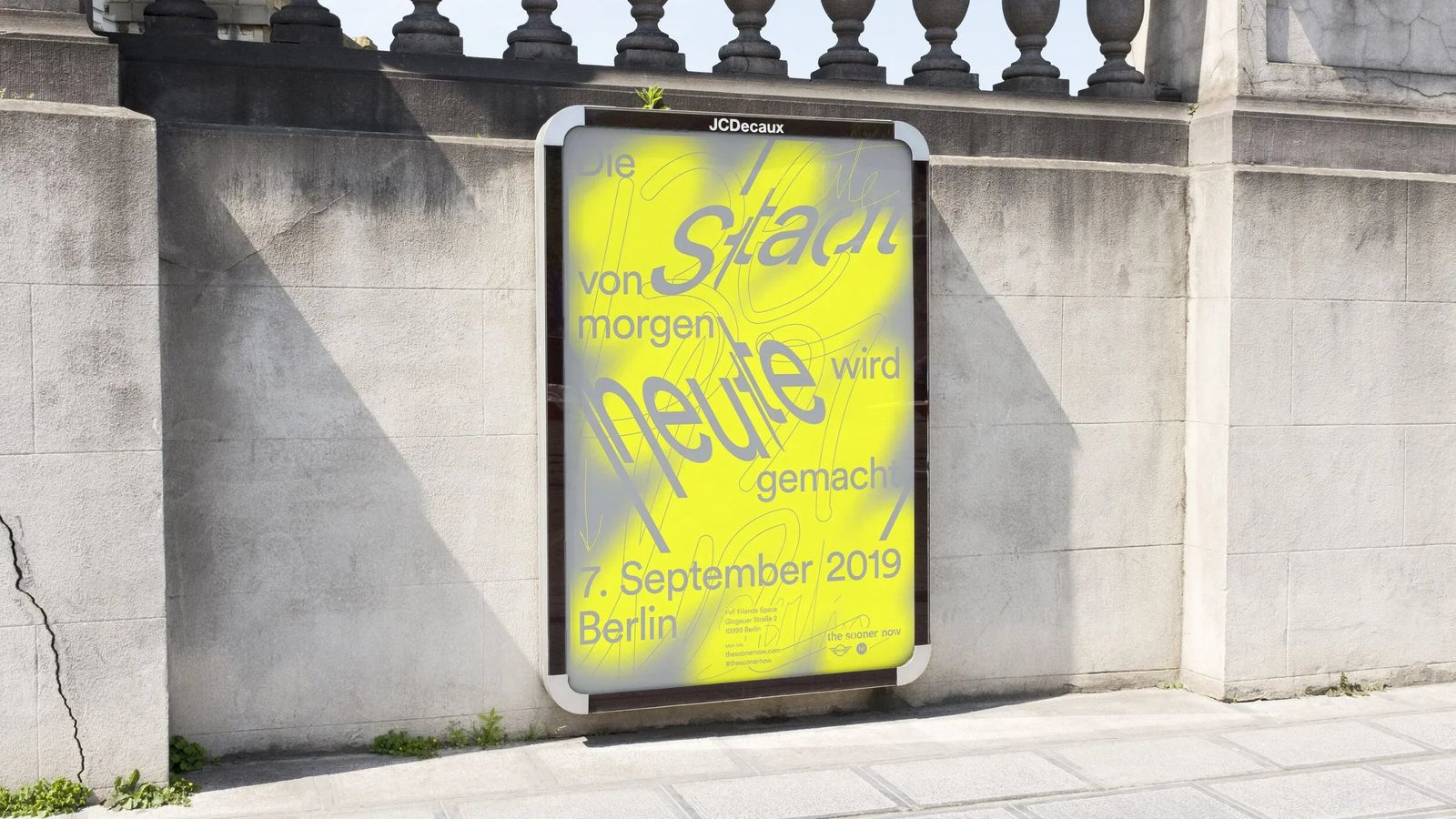 The Sooner Now neon yellow poster on a city billboard against a stone wall