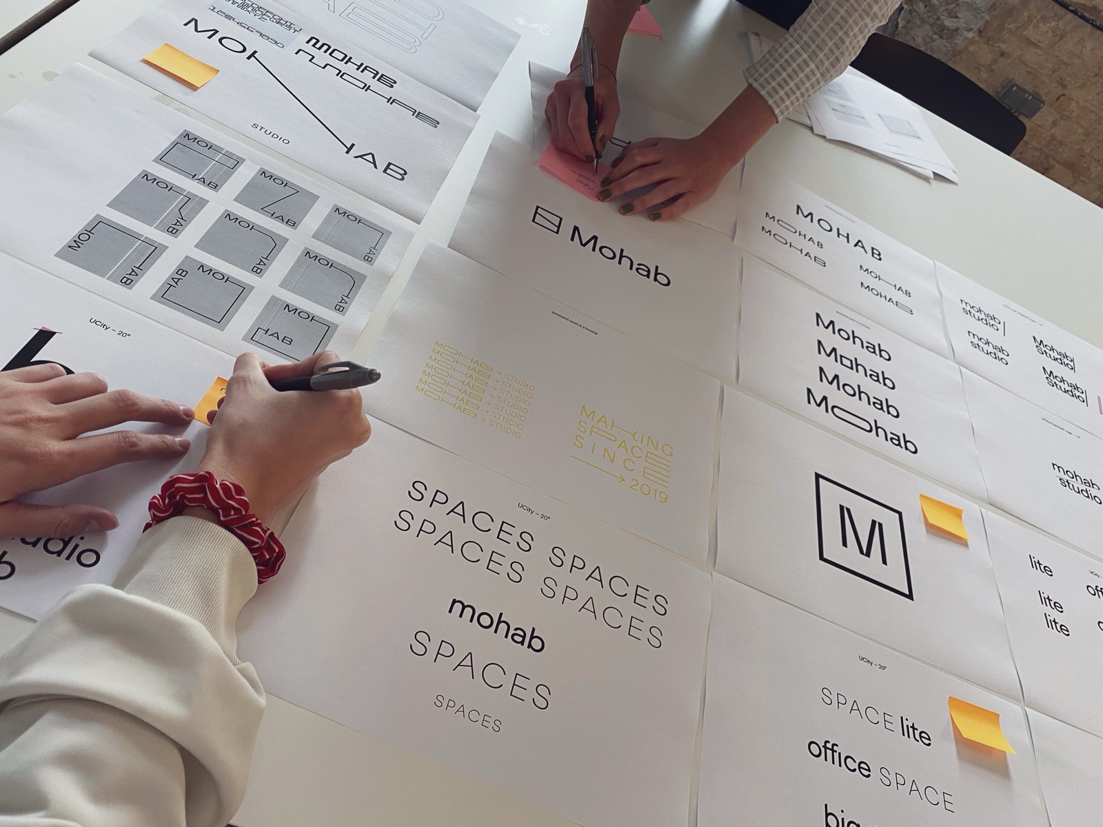 MOHAB logo development, hands sketching wordmark options on printed sheets