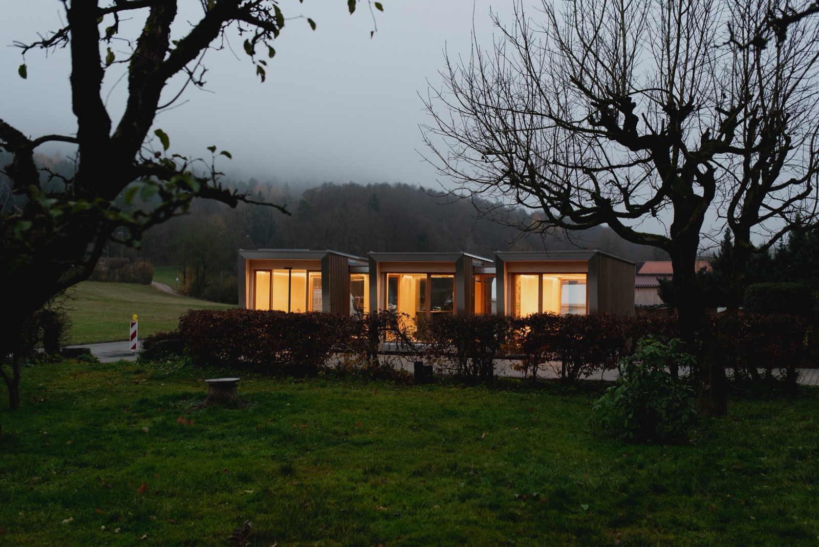 MOHAB Space tiny home lit from inside at dusk in a misty garden