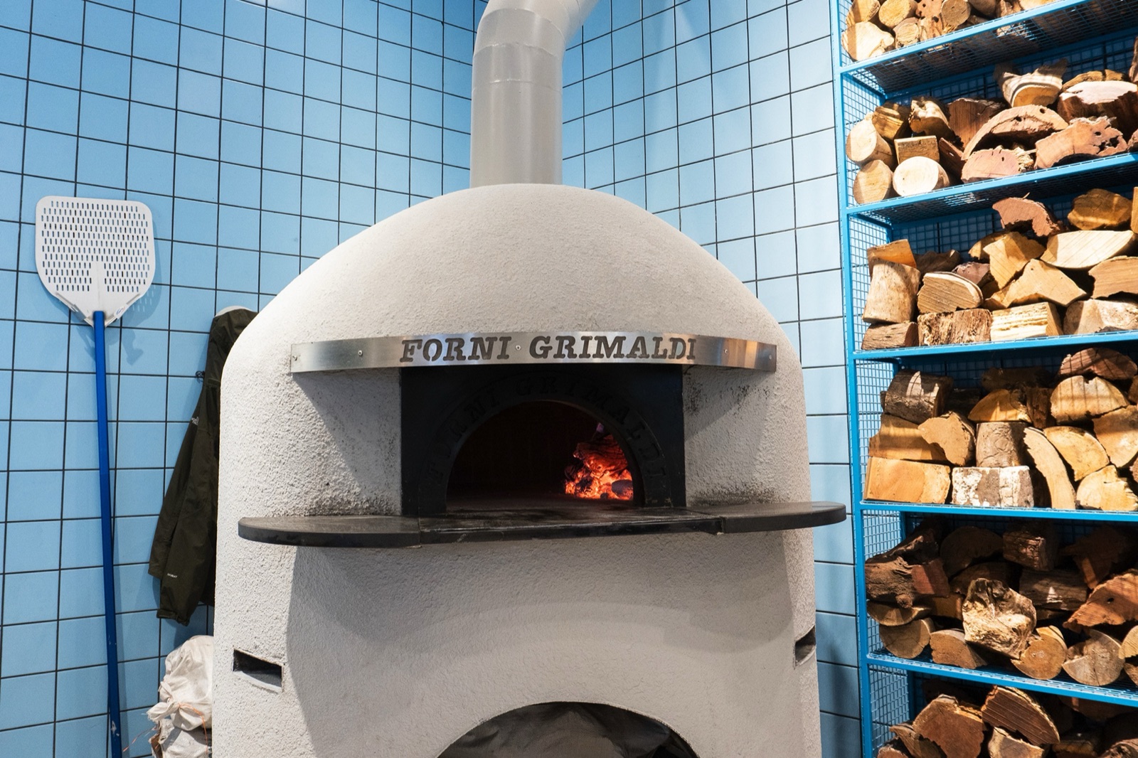 Forni Grimaldi wood-fired pizza oven at ORNO with stacked firewood and blue tiles