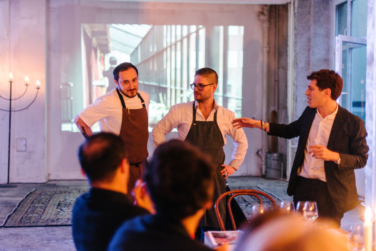 Hosts in aprons giving a toast to seated guests at the Supra dinner
