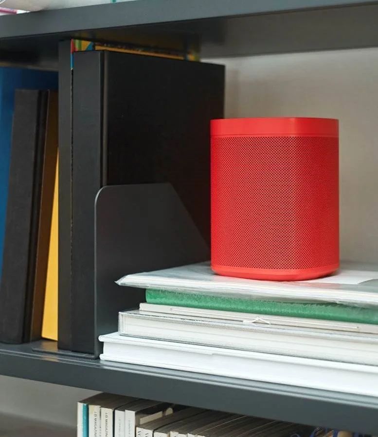 Red HAY x Sonos One on a stack of books on a dark shelf