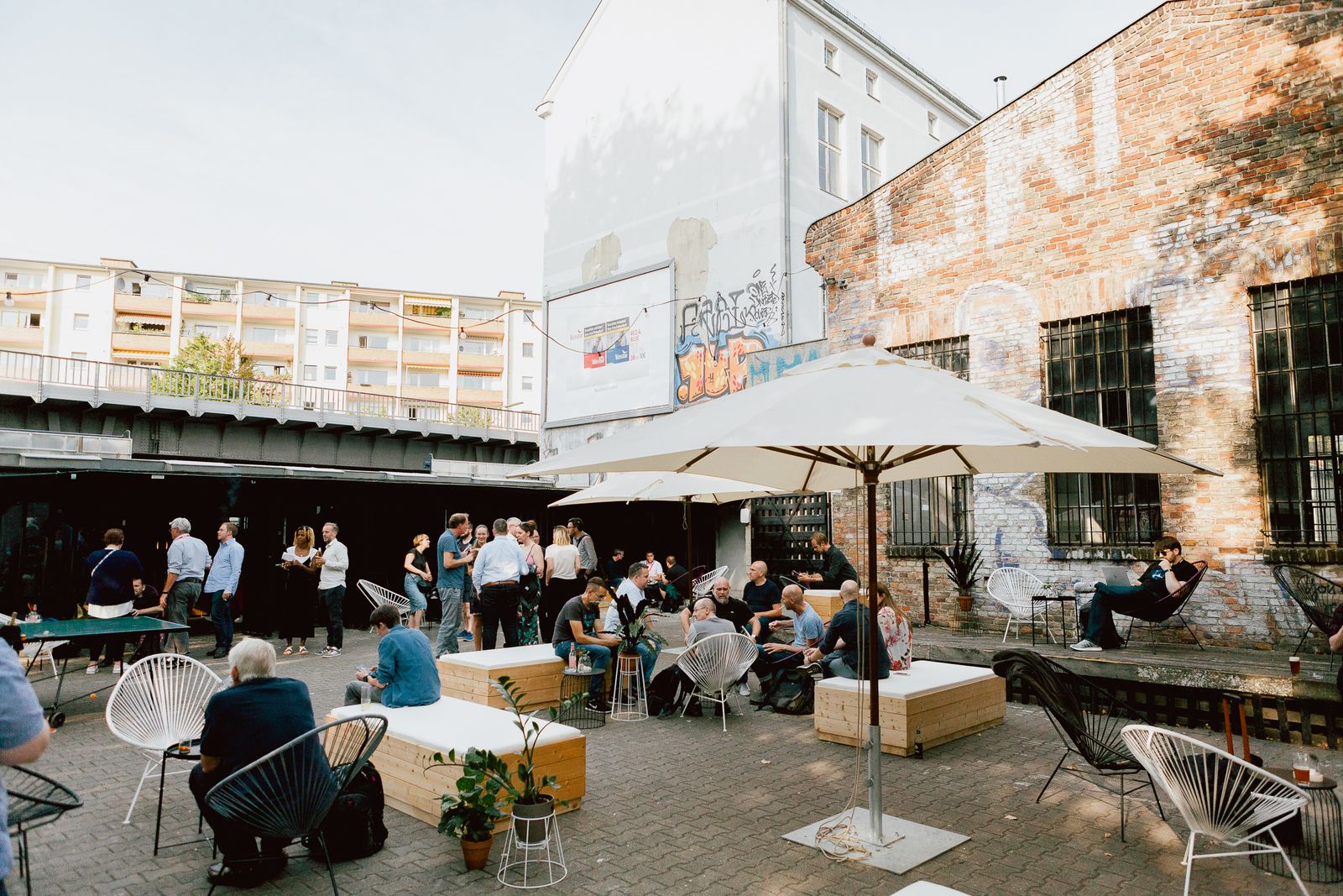 Guests in the brick courtyard of Zwei Drei Raum under white parasols during the Sonos IFA hub