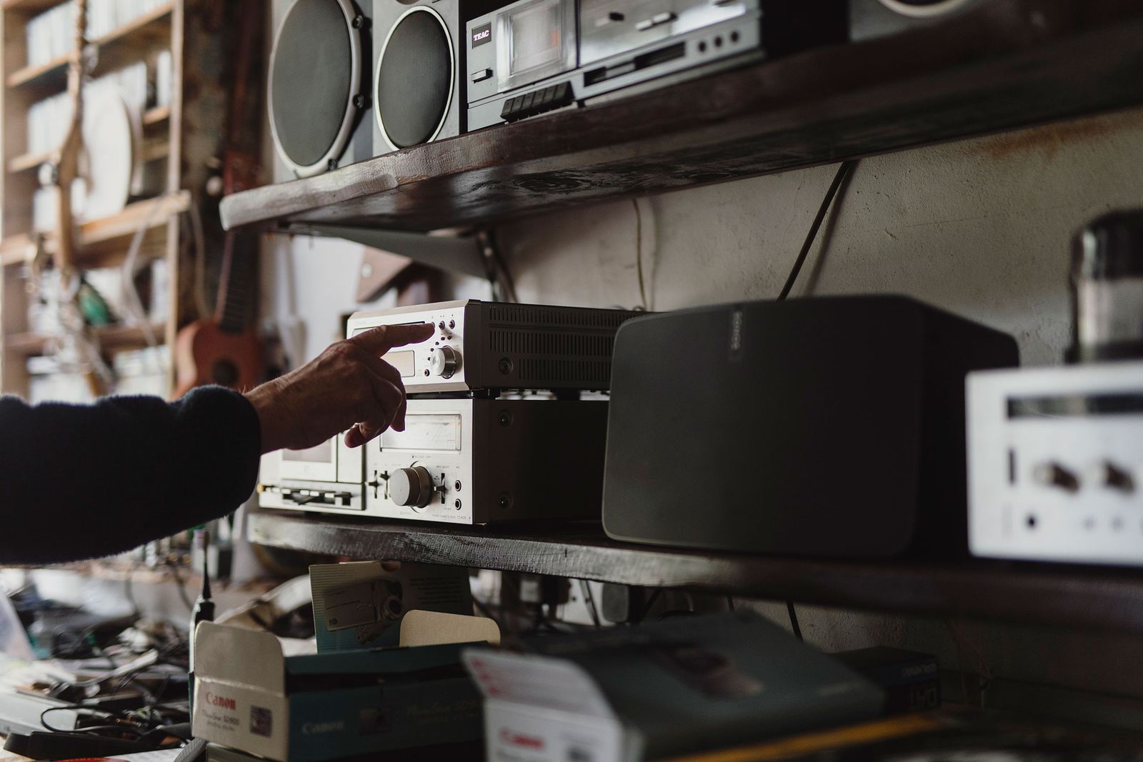 Black Sonos speaker on a studio shelf among radios and audio equipment