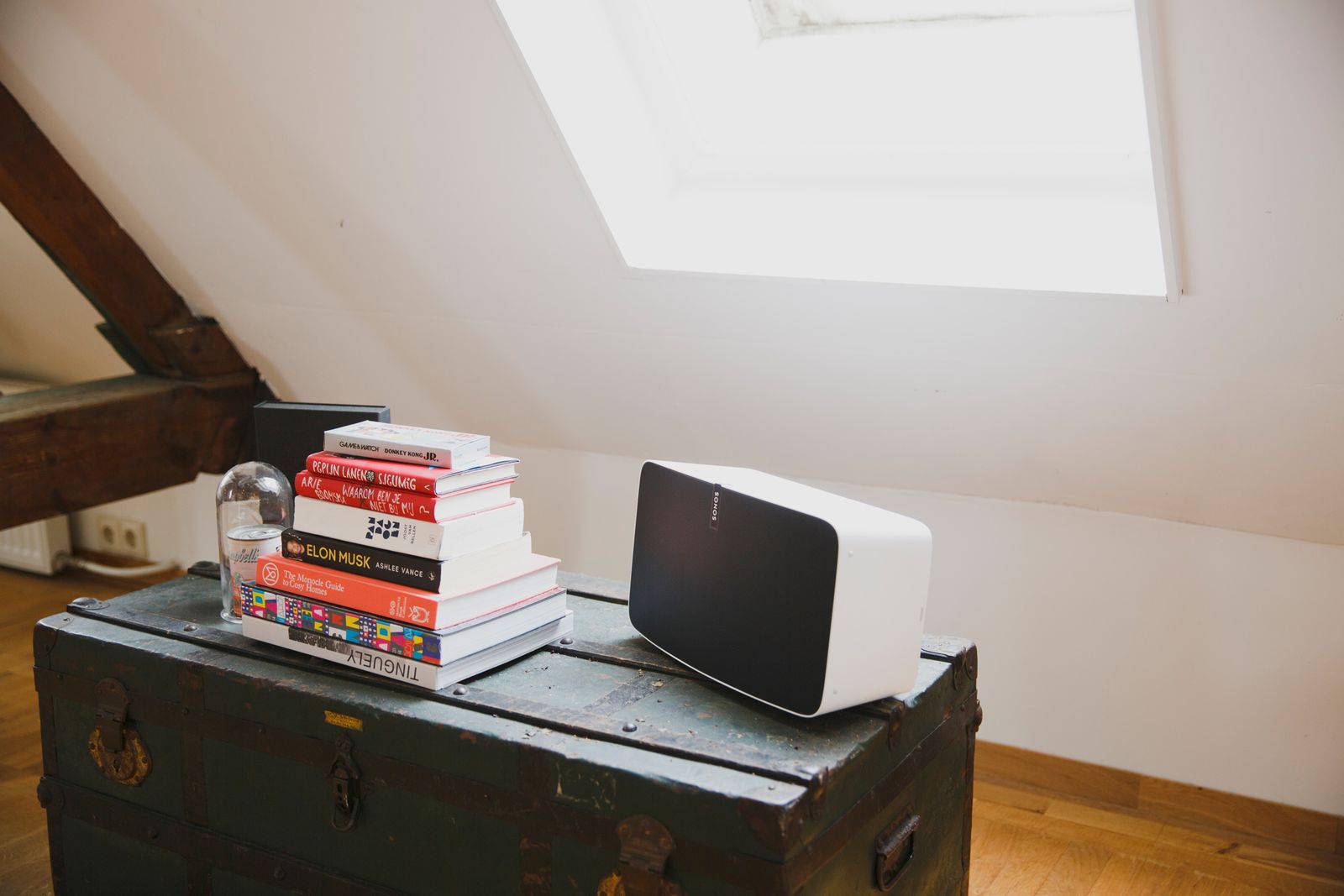 White Sonos speaker and a stack of books on a vintage trunk under a skylight