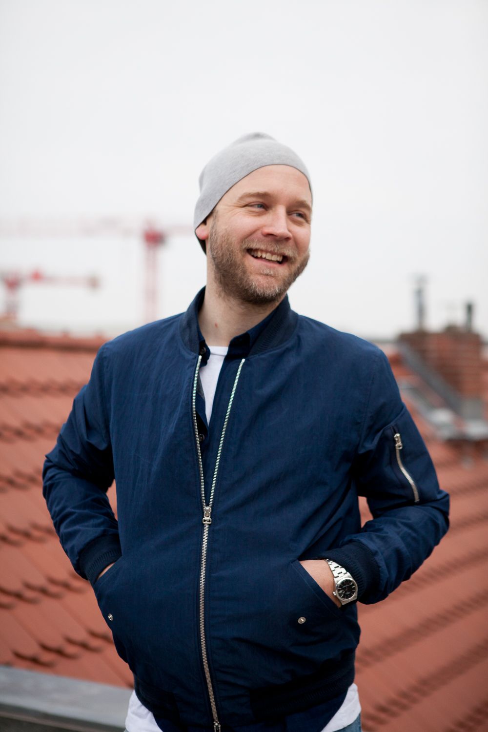 Host in a navy jacket smiling on a Berlin rooftop