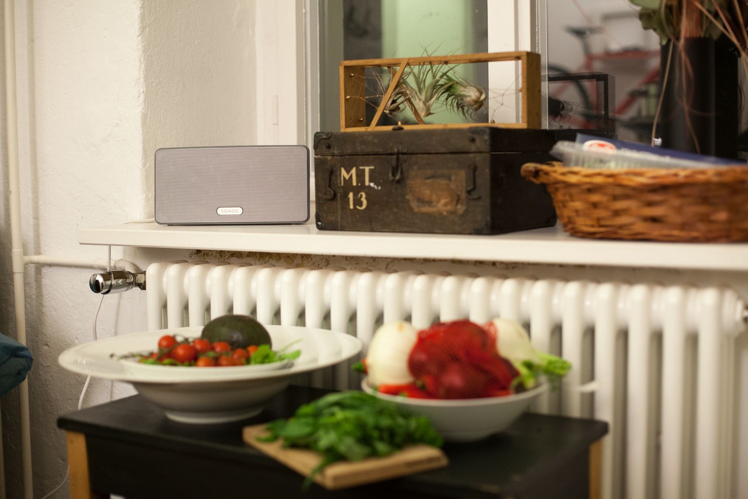 White Sonos speaker on a windowsill above a radiator, with bowls of vegetables below