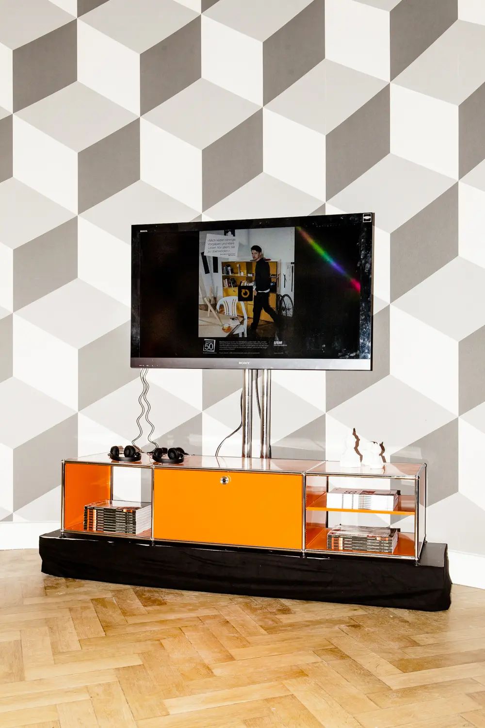 Orange USM Haller unit with a screen in front of grey cube-pattern wallpaper, USM project50 anniversary event