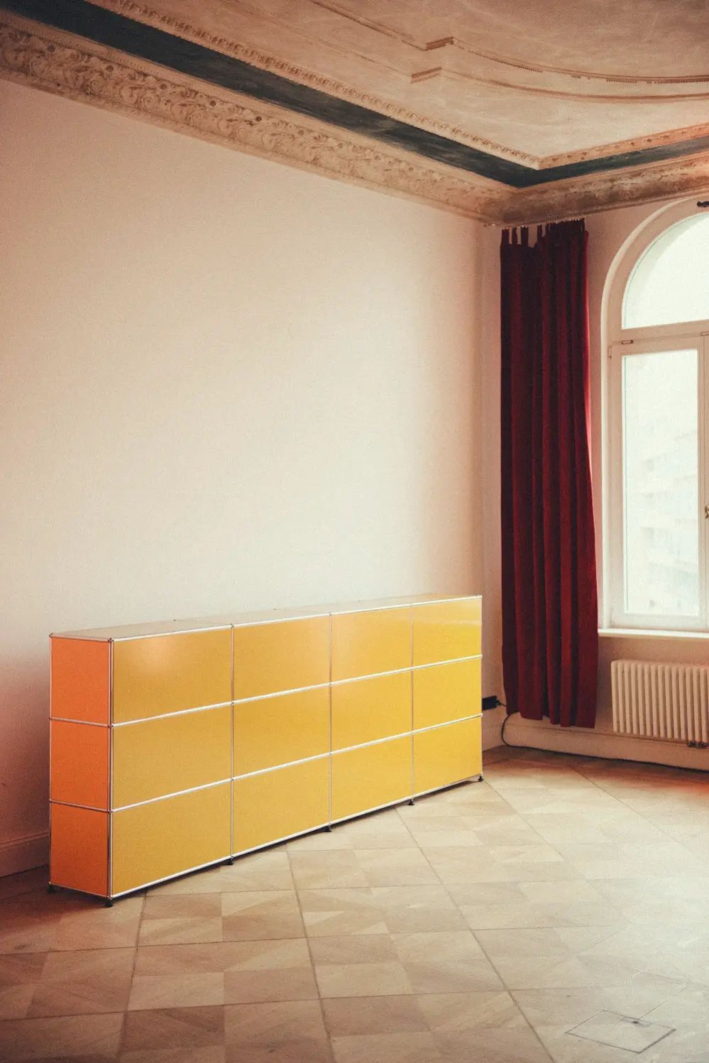 Yellow USM Haller sideboard in an empty Berlin Altbau room with an arched window