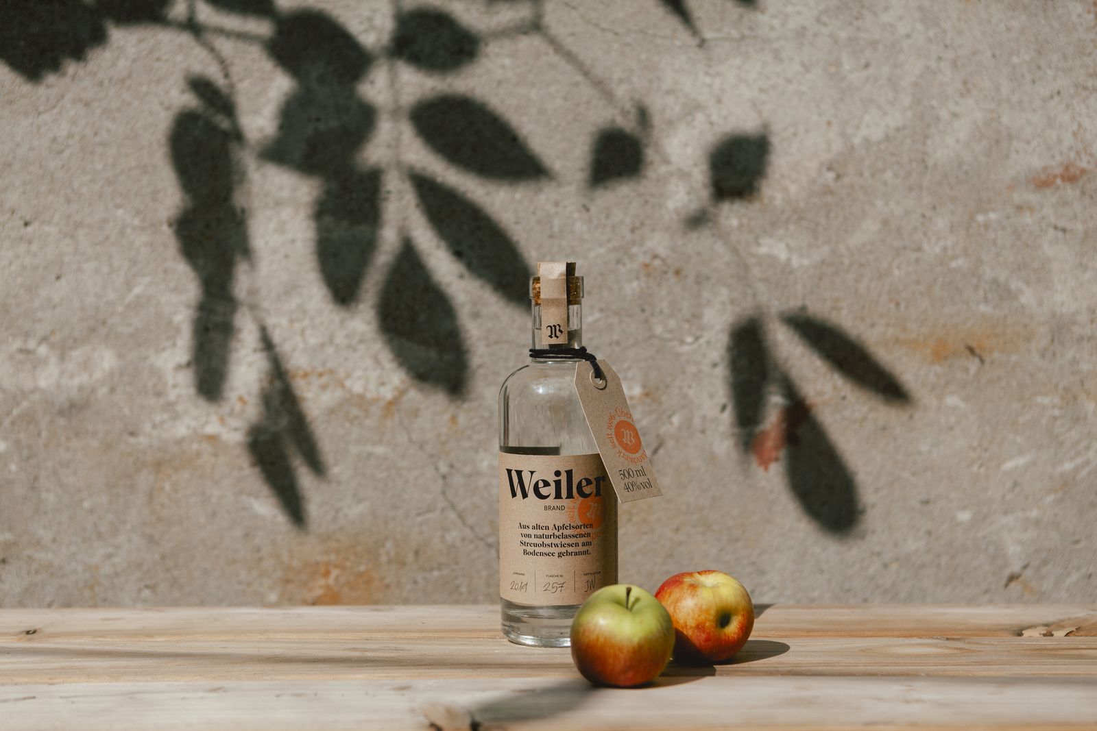 Weiler bottle with two apples, leaf shadows on a concrete wall