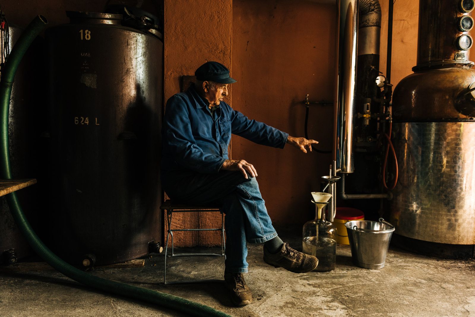 Distiller seated between copper stills in the still house