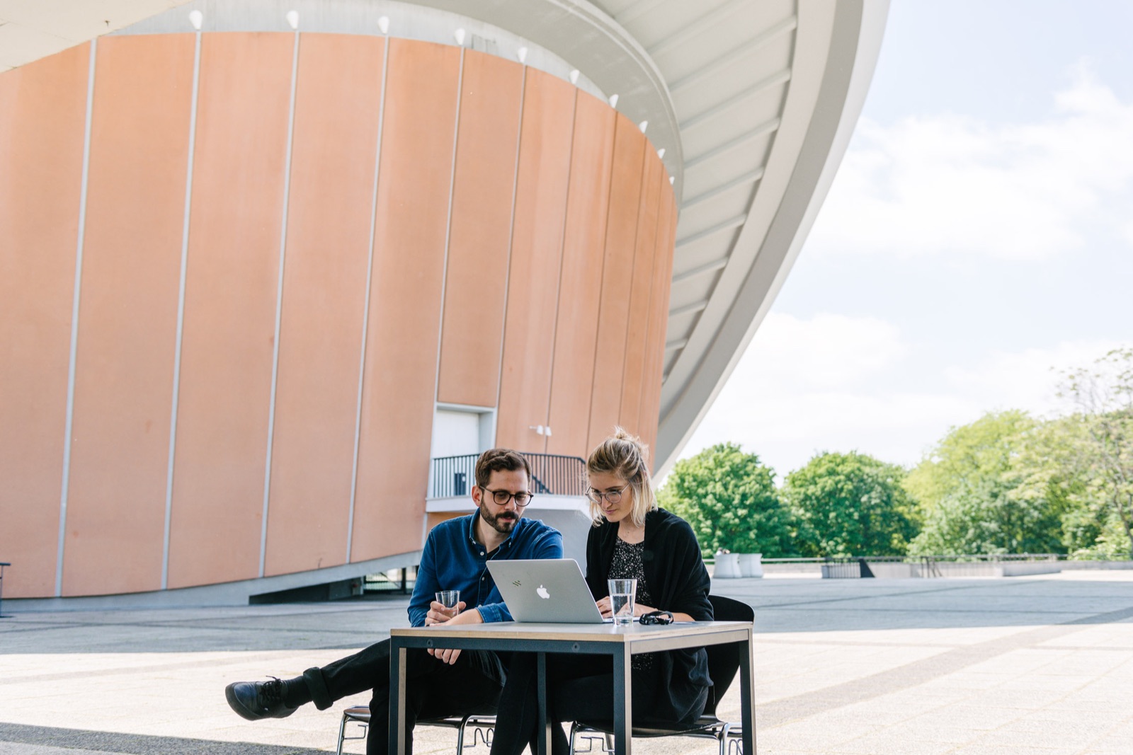 Birgit Palma and Daniel Triendl sharing one laptop at a table outside Haus der Kulturen der Welt