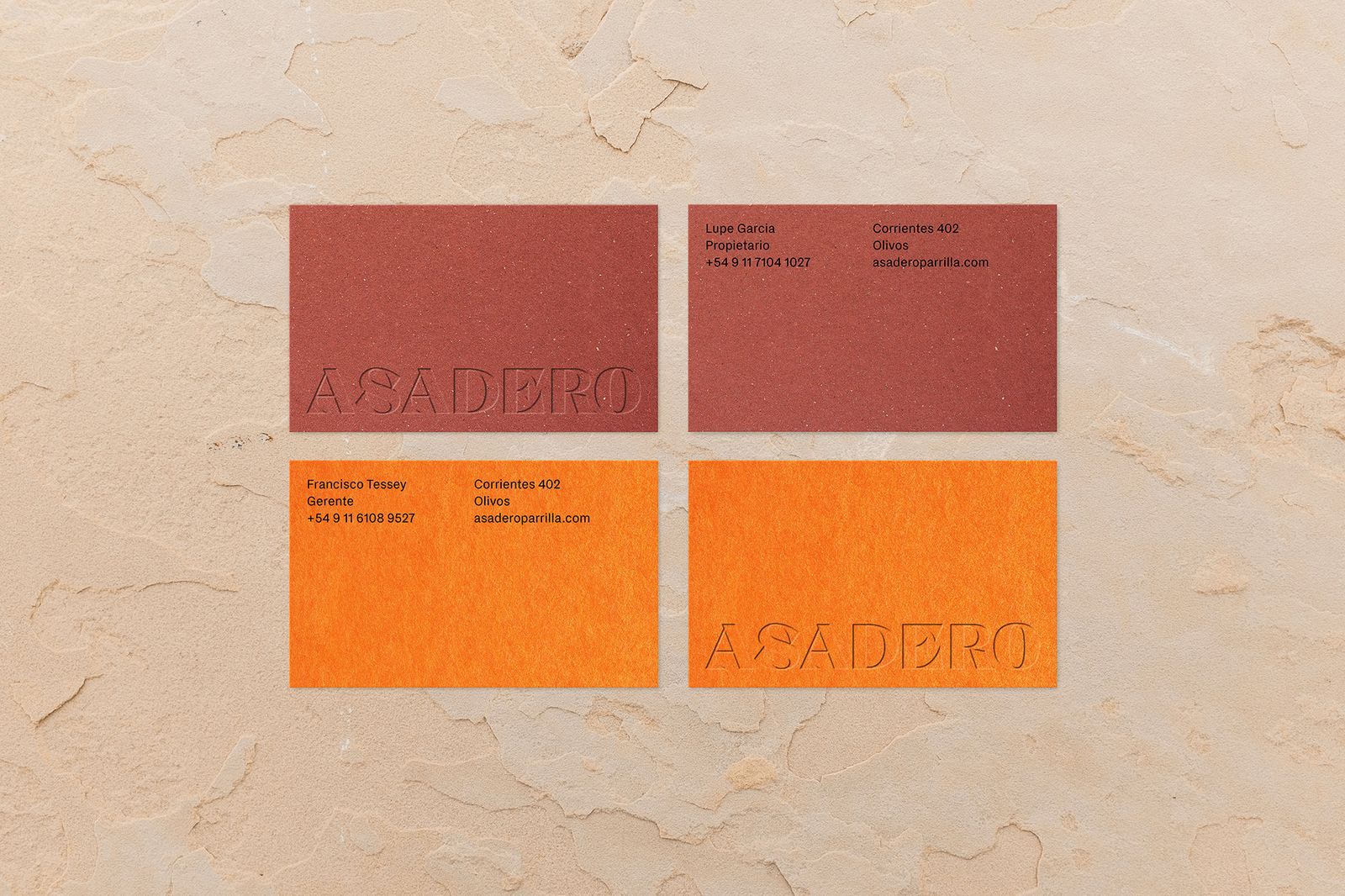 Red and orange Asadero business cards with embossed logo on a plaster surface