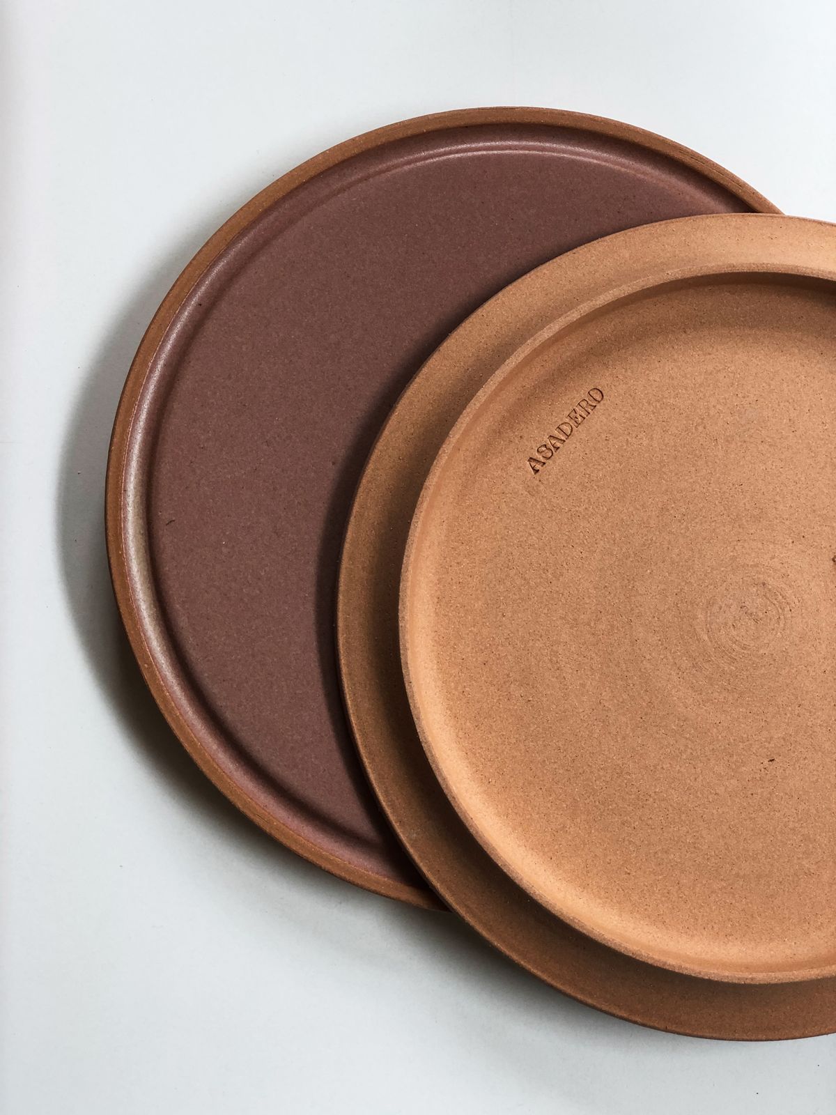 Two clay plates in brown and terracotta stamped with the Asadero logo